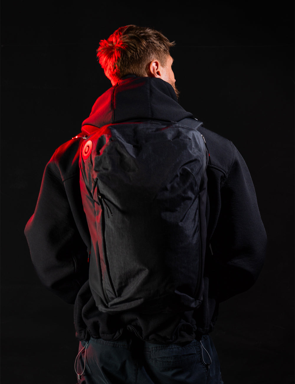 Person wearing a black jacket with red accents on a black background